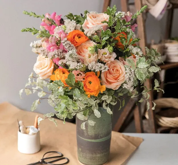 Bouquet de roses pêche, renoncules orange et fleurs roses dans un vase rustique
