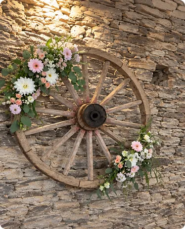 Ancienne roue de charrette fleurie de bouquets roses contre un mur de pierre