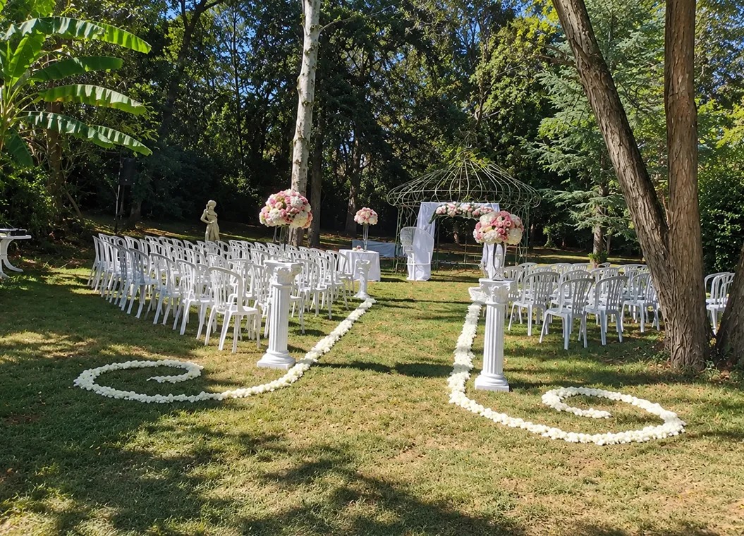 Allée de cérémonie en extérieur bordée de chaises blanches et de pétales
